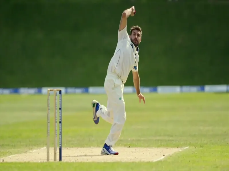 Photograph of a fast bowler mid-stride delivering the ball on a green cricket pitch under daylight