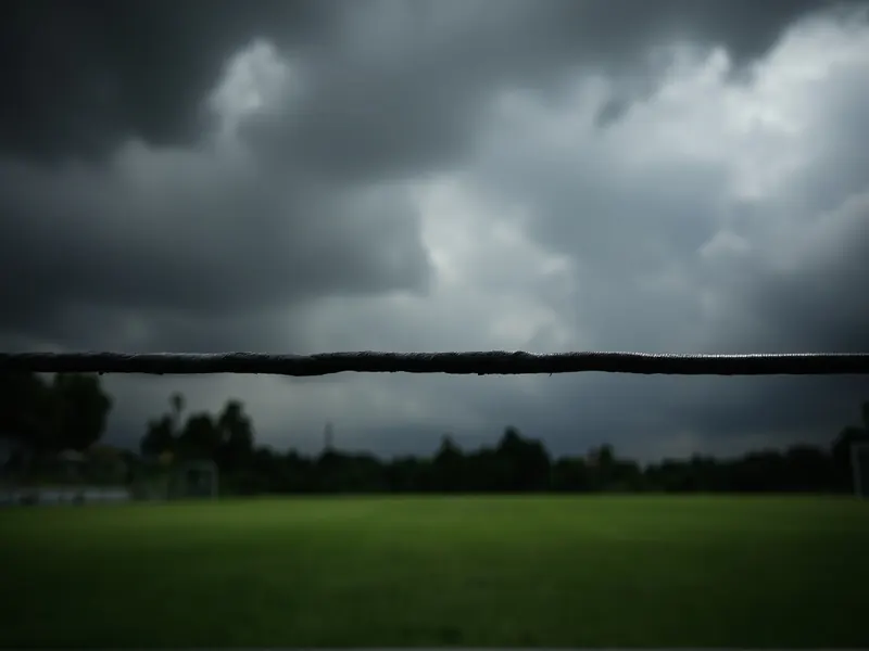 Cricket ground under heavy clouds with the boundary rope dark against green outfield