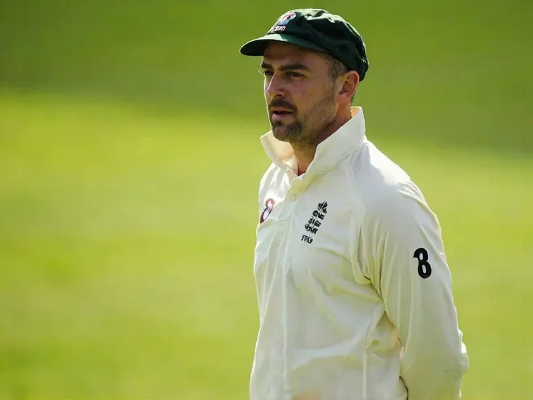 Cricket captain walking out to toss with a folded blazer over the arm, focused expression