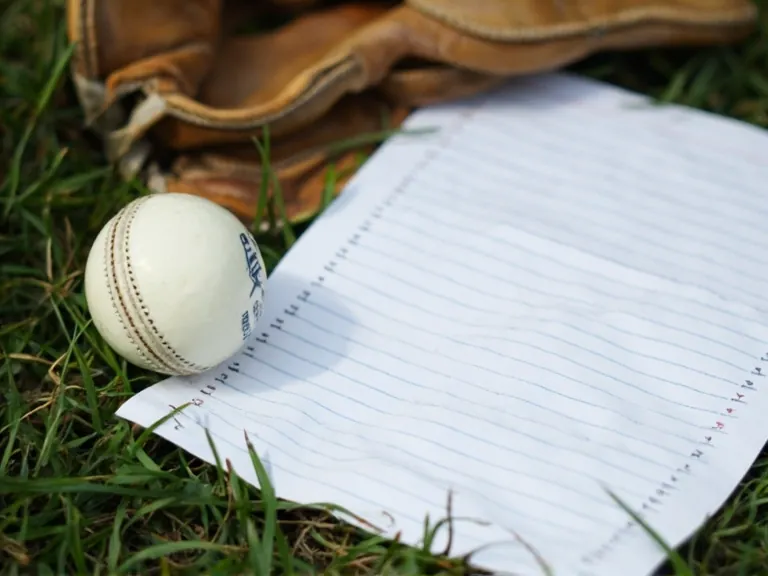 Batting card leaning against an open kit bag on grass, no readable text on the card